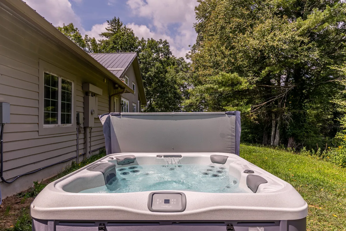 A tranquil exterior scene showcases a bubbling hot tub nestled among lush greenery, with the house in the background. The inviting outdoor space is designed for relaxation and soaking after a productive work day, seamlessly connecting the indoor workspace experience to outdoor leisure.