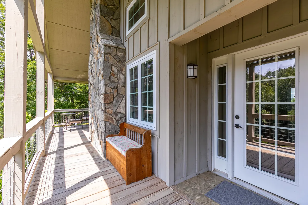 A stone wall framing a wooden bench and double doors that open out to a generous porch, with large windows providing views of the surroundings. The space is designed for enjoying sunsets and quiet moments, blending the indoors with the outdoors.