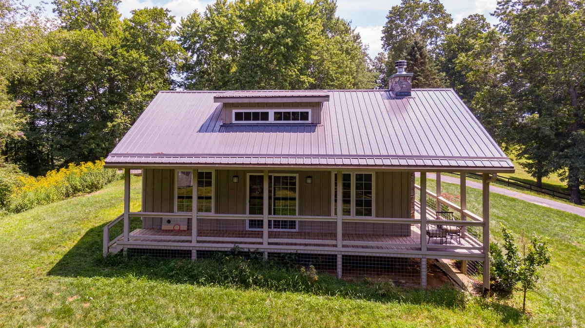 A peaceful front porch with a metal roof and large windows, surrounded by greenery. The porch offers a comfortable spot to take breaks, enjoy sunrise coffee, or simply soak in the serenity of the High Country.