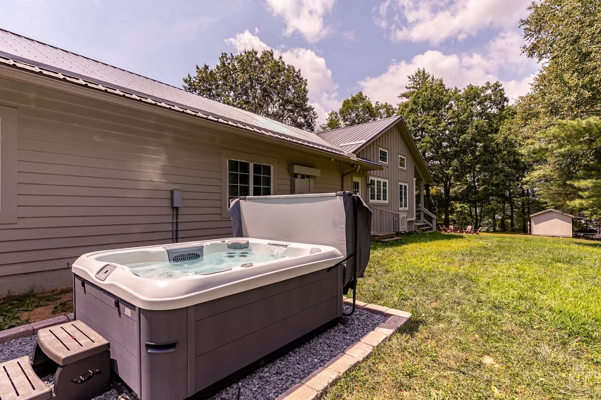 The hero image showcases the inviting exterior of a single-family house nestled among lush North Carolina trees, with a sparkling hot tub taking center stage on a spacious patio. The scene suggests opportunities for outdoor relaxation, gatherings, and close connection to nature, all in a tranquil riverside setting.