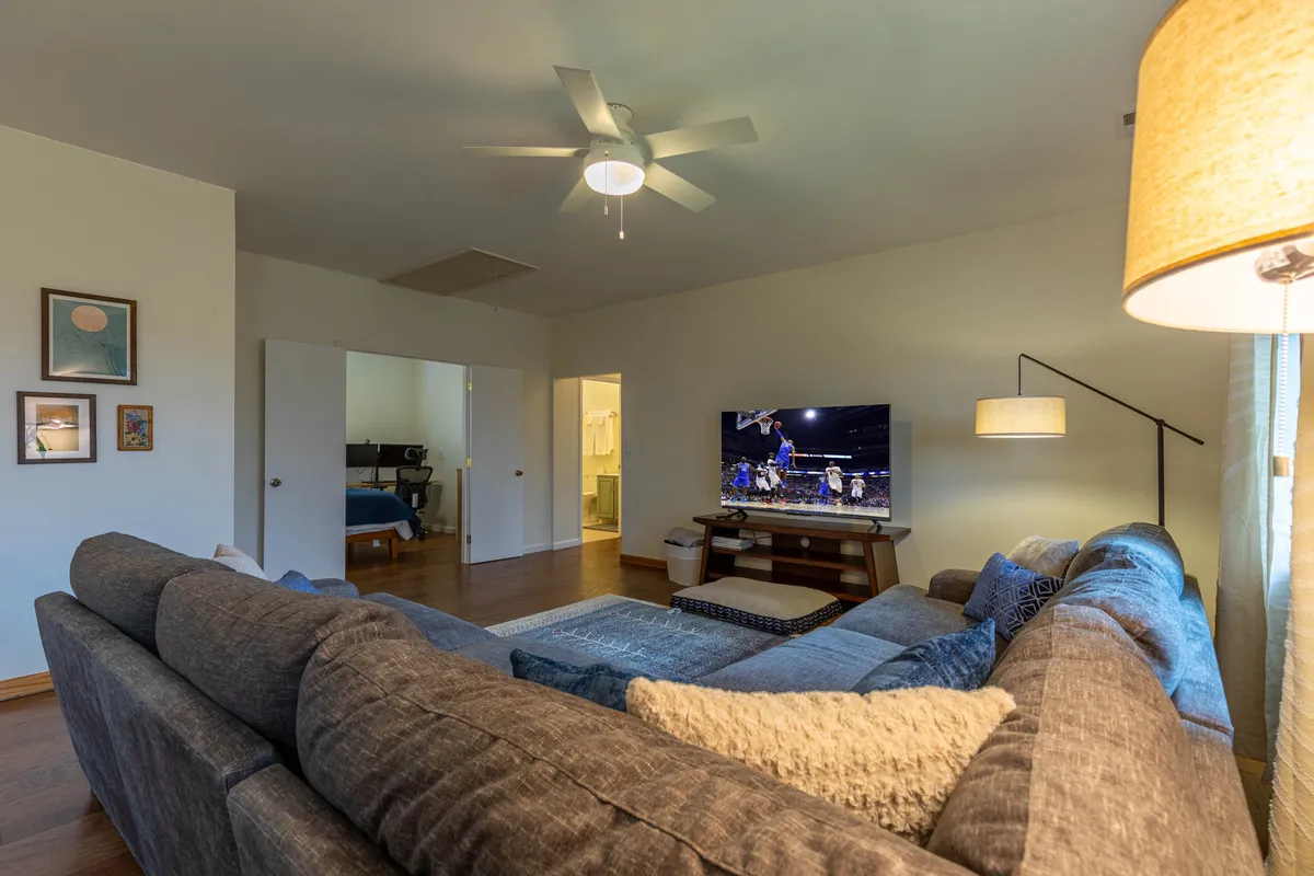 A spacious living area anchored by a large sectional sofa facing a wall-mounted television. Thoughtful decorative touches, such as a sleek lamp and framed artwork, create a comfortable, family-friendly atmosphere ideal for movie nights or quiet evenings in.