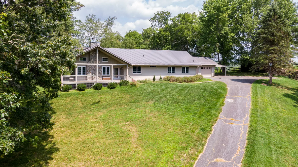 A welcoming view of the house's front porch with a landscaped lawn and driveway, framed by natural scenery. The setting evokes a sense of arrival and anticipation for adventure or relaxation.