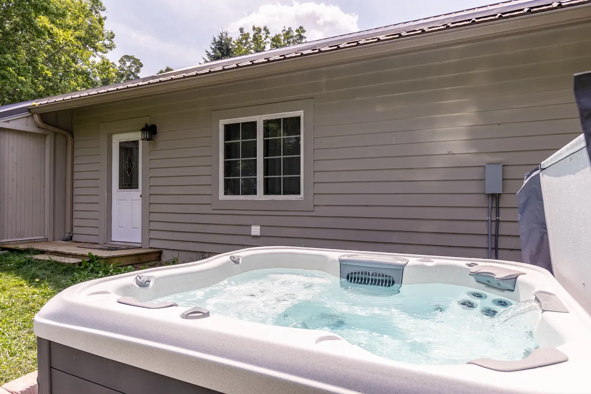 A secluded outdoor hot tub set just outside the house, framed by nature and glimpses of the back door. The setting is ideal for unwinding after a productive workday, offering privacy and relaxation under open skies.